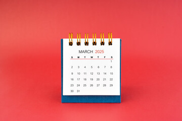 March 2025 white desk calendar on red background.