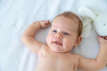 A newborn baby lies on a white background with a soft toy bunny. baby