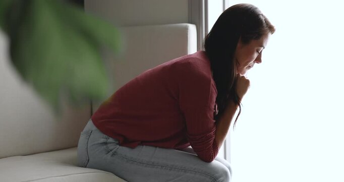 Sad young woman overcome hard period of her life, sitting alone on sofa thinks with eyes closed, calming herself during panic attack suffers from unstable psyche or mood. Mental disorder, need support