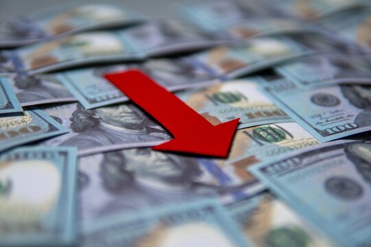 A red arrow pointing downwards on top of a pile of US dollar bills. Economic recession, financial decline, economic downturn concept.