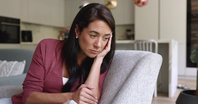 Upset young woman sits on sofa at home looks insulted and frustrated, having problems in relationships, thinks on divorce, suffers from break up, separation, marriage split. Nostalgic mood, solitude