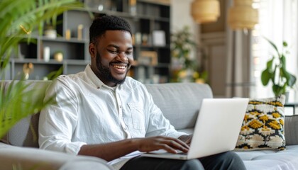Obraz premium Happy african american man working from home using laptop on sofa is smiling