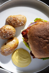 Beef burger with potatoes on white plate. Homemade burger with bacon. Close-up of home dinner