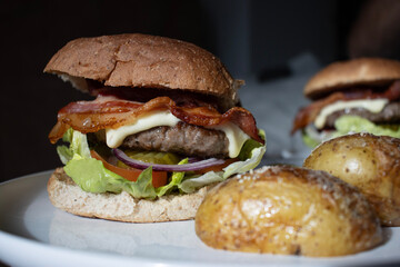 Beef burger with potatoes on white plate. Homemade burger with bacon. Close-up of home dinner