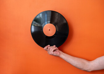 Male hand holding vinyl record on background of orange wall.