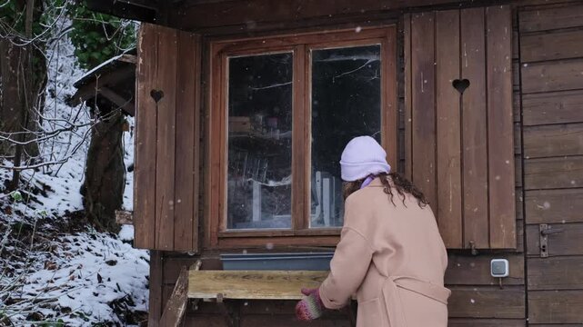Curious caucasian woman explore an abandoned wooden cottage, carefully watching inside through the window. Nosy neighbour stalking or snooping secrets, gossip and rumour. Stalker peeping people.