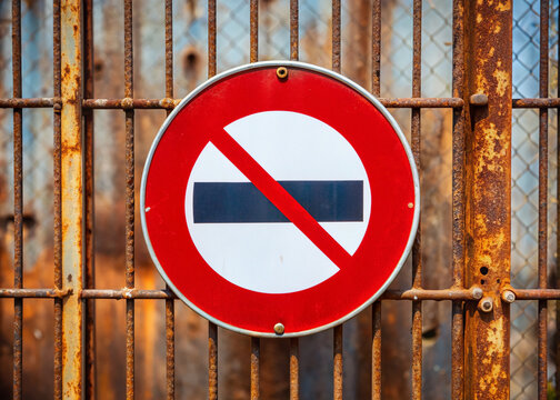 Forbidden access sign with bold red circle and white diagonal stripe, mounted on a rusty metal gate, conveying a strong message of restriction.