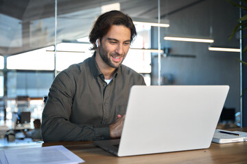 Happy business man hr manager professional executive in earbuds working in office looking at laptop...