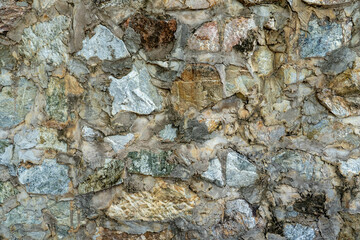 A rough stone wall made of large gray pieces of stone filled with cement mortar.