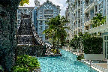 An artificial cascade of a waterfall whose water falls into a pool of blue water among tropical vegetation. At the edge of the pool there are metal stairs to get into the water.