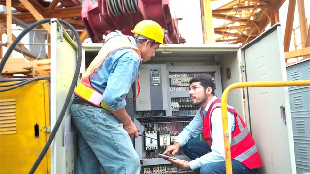 Bothe of electrical engineer inspects the electrical control board of a crane before putting it to use on a construction site