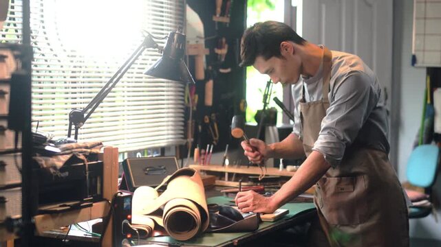 Professional male artisan using a hammer and other tools to shape and detail the leather piece in the workshop