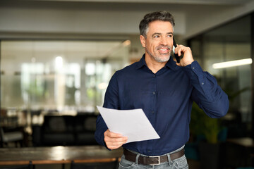 Busy older business man hr manager of middle age making call in office. Mature senior businessman executive, lawyer or entrepreneur holding documents talking on the phone at work consulting client.