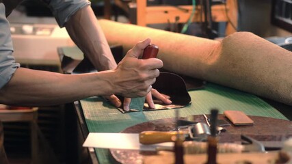 Slow motion of young craftsman cutting leather parts at table in his workshop studio