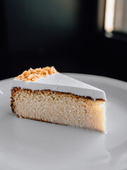 delicious piece of cake with white cream frosting, chocolate, and flavorful sponge on a beautiful plate in a cozy nice restaurant