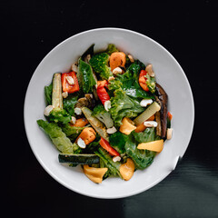 delicious salad with juicy tomatoes, fresh vegetables, and fragrant herbs on a beautiful white plate on a black table in a cozy nice restaurant