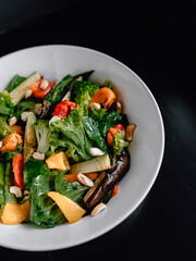 delicious salad with juicy tomatoes, fresh vegetables, and fragrant herbs on a beautiful white plate on a black table in a cozy nice restaurant