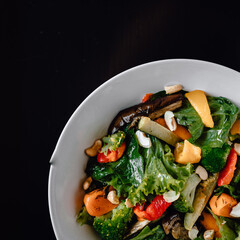 delicious salad with juicy tomatoes, fresh vegetables, and fragrant herbs on a beautiful white plate on a black table in a cozy nice restaurant