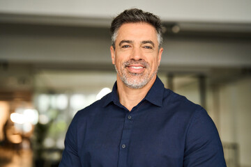 Fototapeta premium Headshot portrait of happy mature professional business man of mid age standing in office. Smiling 50 years old professional business owner manager, senior male ceo executive leader looking at camera.