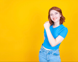 This is it! I win! Young beautiful red bob hair woman clenched fist up air biting lips blink an eye standing over yellow studio background copy space. Winner celebrating concept design idea.