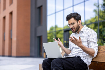 Frustrated man working on his laptop outside office building