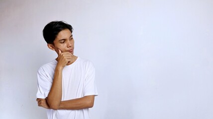 Asian young man thinking wearing white shirt while looking to the right side