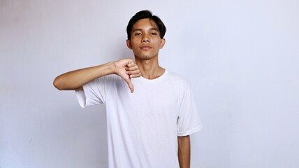 Asian young man wearing white shirt gesturing thumbs down