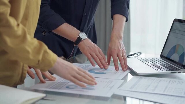Business team analyzing financial charts on desk. Professionals discussing data at a workstation with laptops and documents. Audit and finance concept