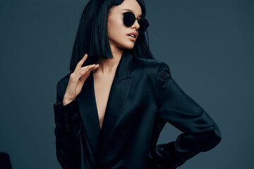 Asian woman in black suit and sunglasses posing against a dark background, showcasing elegance and...