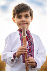 Portrait of little boy child with woodwind wooden flute - ukrainian sopilka, tylynka on sky...
