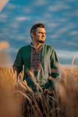 Ukrainian man in vyshyvanka shirt, traditional ornament standing in wheat field