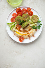 White plate with hummus, falafel and vegetables, flat lay on a light-beige stone background, vertical shot with copy space