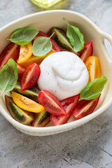 Burrata cheese with heirloom tomatoes and green basil in a beige serving tray, vertical shot on a grey granite surface, middle close-up