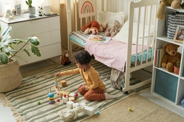 Young child playing with colorful blocks on carpeted floor in cozy bedroom filled with toys and...