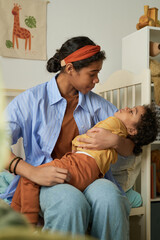 Mother holding her child in cozy bedroom, showing tender affection and nurturing care. Child looking up at the mother with admiration and comfort