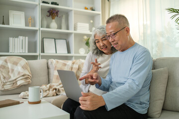 Obraz premium Loving elderly couple using laptop while sitting together on a cozy sofa in a bright living room.