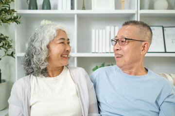 Happy elderly couple sitting on sofa look at each other with a loving gaze.