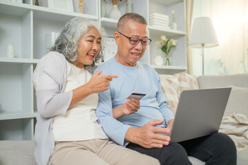 Happy mature couple holding plastic credit card and using laptop, making payment, shopping online or booking hotel.