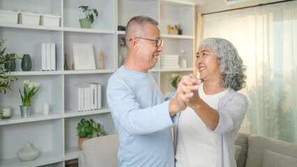 Fototapeta premium Loving elderly couple happily dancing together in a cozy living room, enjoying a tender moment and smiling warmly at each other.