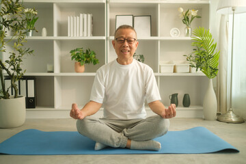 Fototapeta premium Serene mature man practicing yoga while sitting in lotus position on mat at home. Elderly and healthy lifestyle concept.