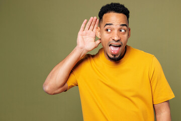 Young curious nosy man of African American ethnicity he wearing yellow t-shirt casual clothes try to hear you overhear listening intently isolated on plain pastel green background. Lifestyle concept.