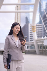 Young professional woman is walking outdoors in a modern urban environment, focused on her smartphone.