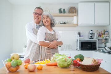 Affectionate elderly couple standing in a bright kitchen, embracing each other warmly and smiling at the camera. Togetherness, healthy lifestyle and retirement lifestyle concept.