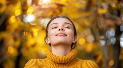 Fototapeta premium A woman in a yellow sweater enjoys nature with her eyes closed against the backdrop of an autumn forest.