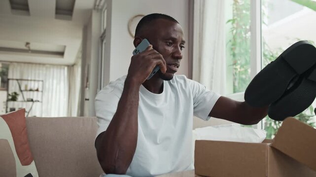 Medium shot of male African American customer talking to support service on mobile phone when getting wrong shoes in parcel