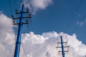 Electricity power pole with transmission lines against blue sky and clouds.