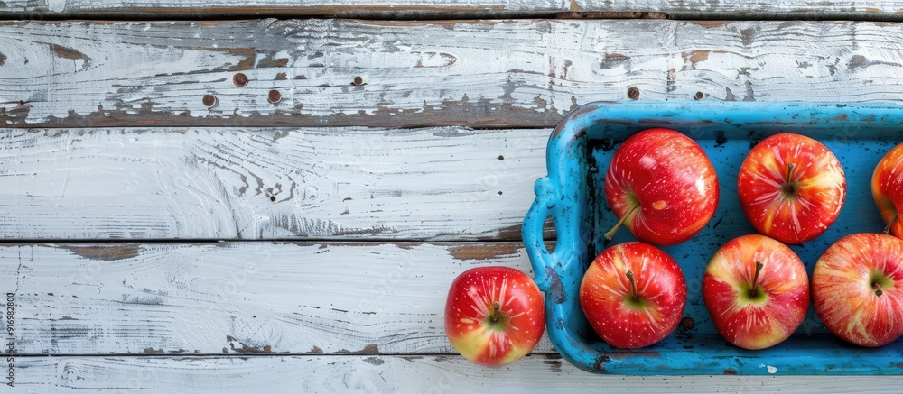 Poster fresh apples arranged neatly on a blue tray on a rustic white wooden table providing a scenic copy s