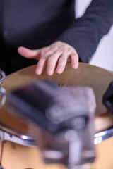 A close-up shot of a hand playing a conga drum, capturing the focus and intensity of the musician, with the drumhead and surrounding instruments slightly blurred in the background.