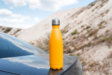 Steel thermo water bottle of yellow color on the car trunk.