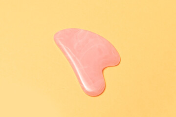 Close-up of guasha face massage of pastel pink color isolated on yellow background.